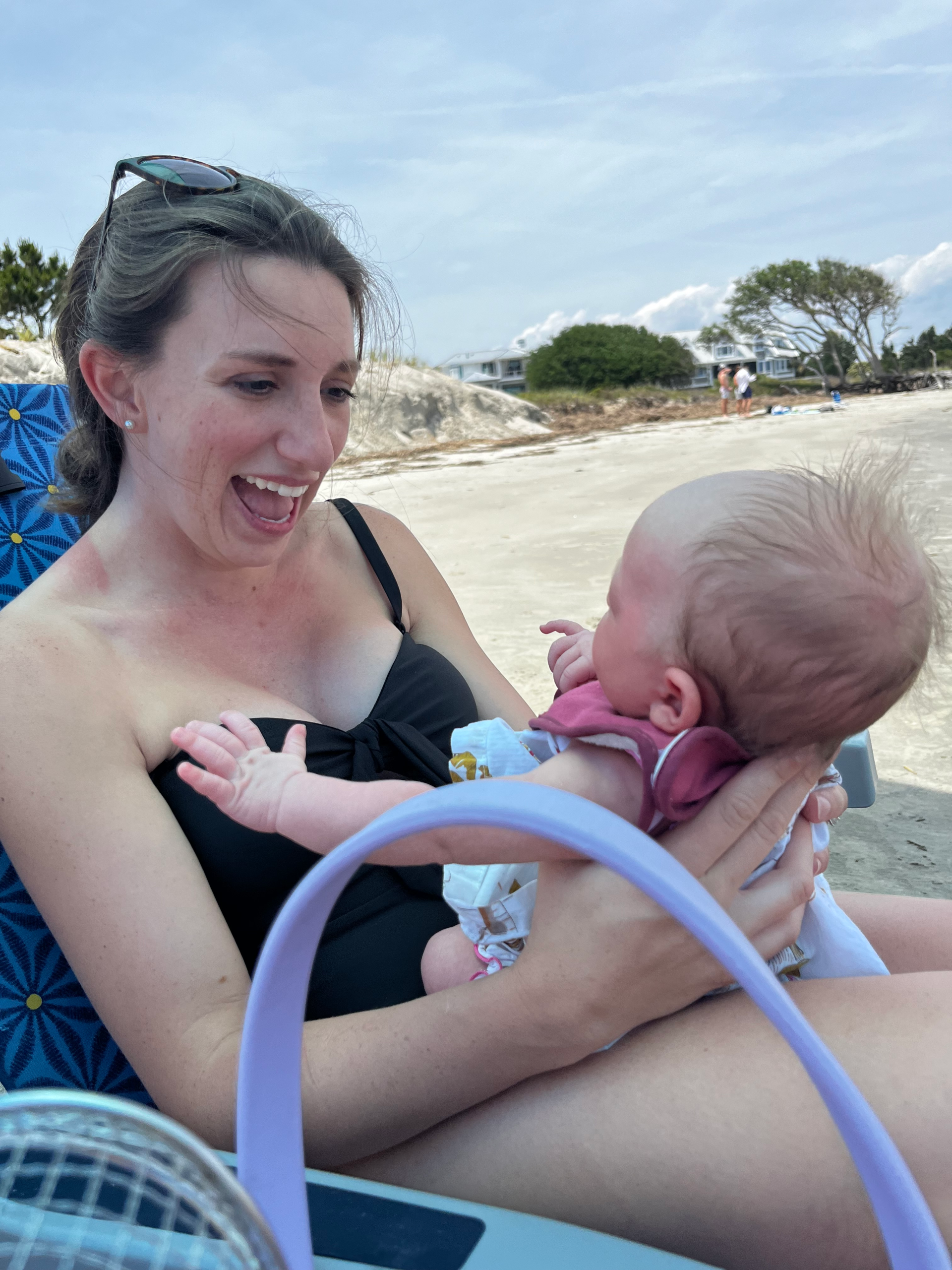 Mom holding newborn baby in beach chair at beach.